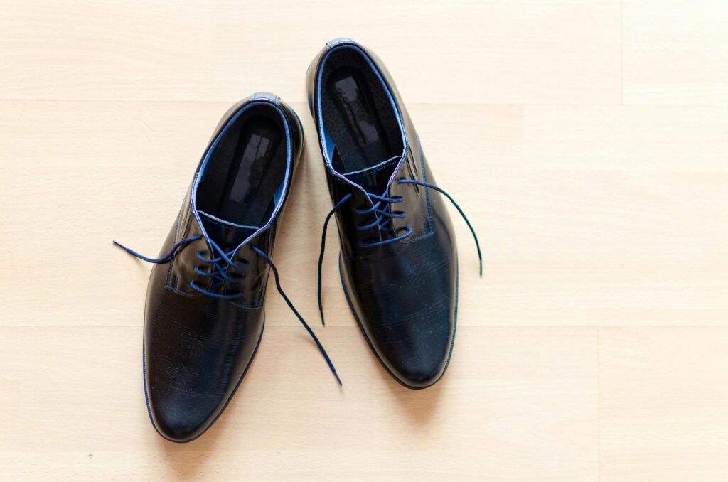 Pair of stylish black leather shoes with blue laces on a wooden floor.